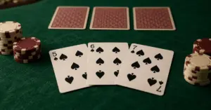 Kolme avointa patakorttia ja pelimerkkejä vihreällä pokeripöydällä, taustalla jakajan kolme kuvapuoli alaspäin olevaa korttia.